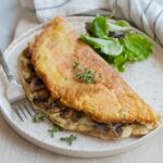 Fluffy omelet filled with mushrooms and cheese on a white plate.