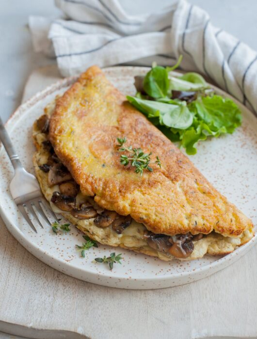 Fluffy omelet filled with mushrooms and cheese on a white plate.