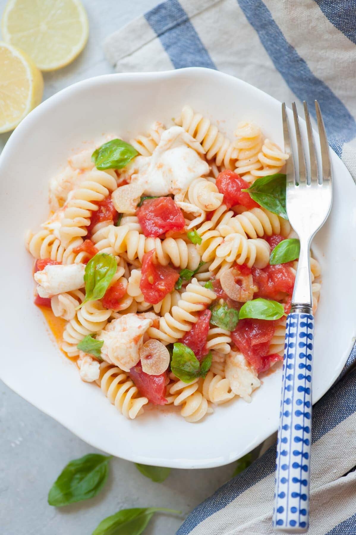 Pasta Caprese in a white bowl with blue fork on the side.