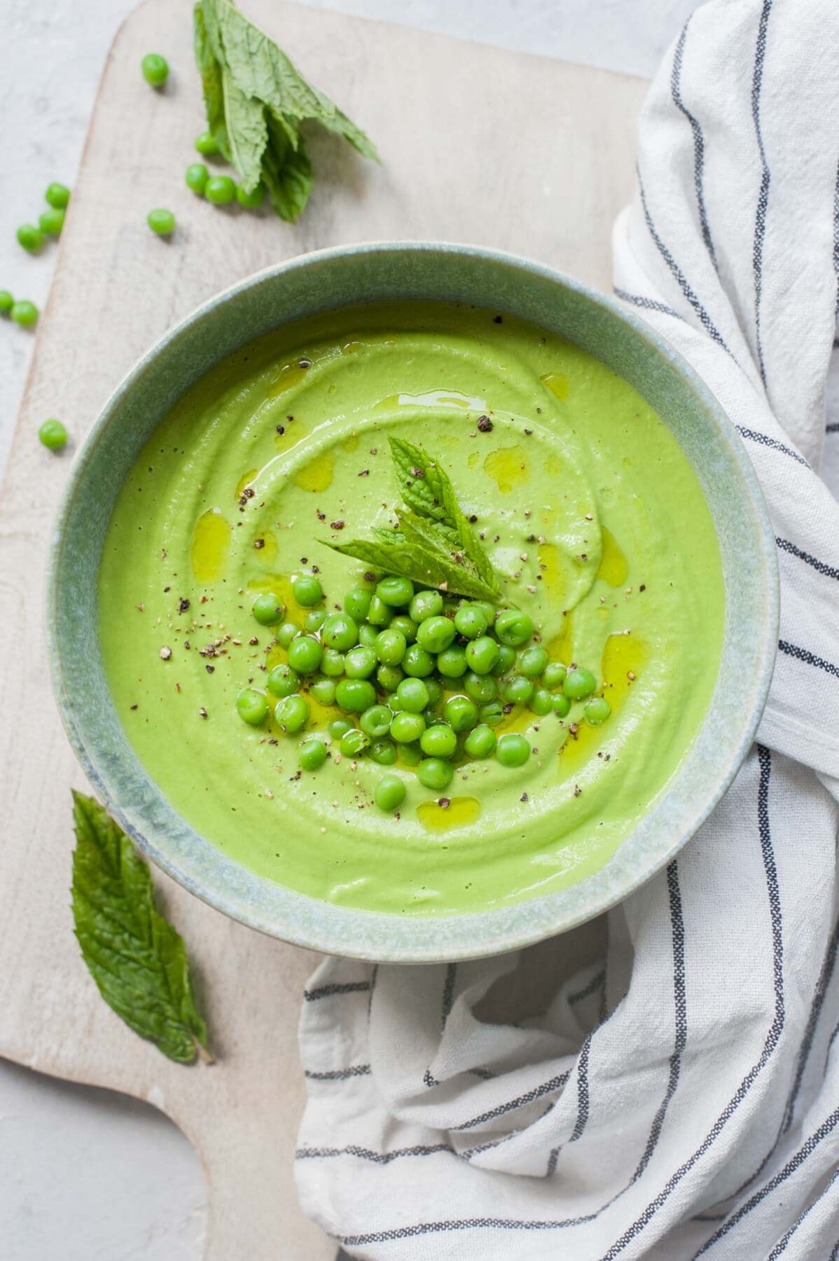 Pea mint puree in a green bowl topped with peas and mint leaves.