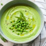 Pea mint puree in a green bowl topped with peas and mint leaves.