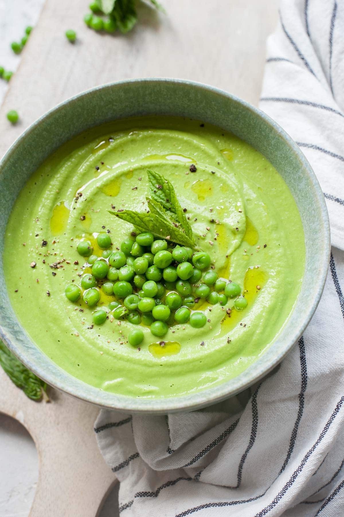 Pea mint puree in a green bowl topped with peas and mint leaves.