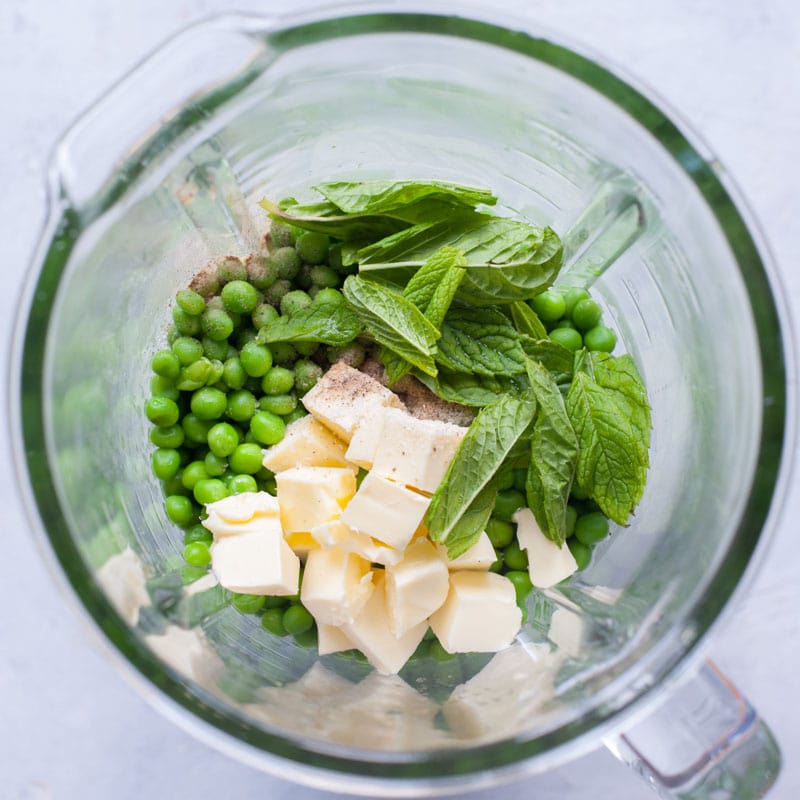 Cooked peas, mint leaves and butter in a blender bowl.