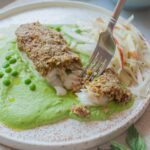 Pistachio crusted fish with mint puree and kohlrabi slaw on a white plate.