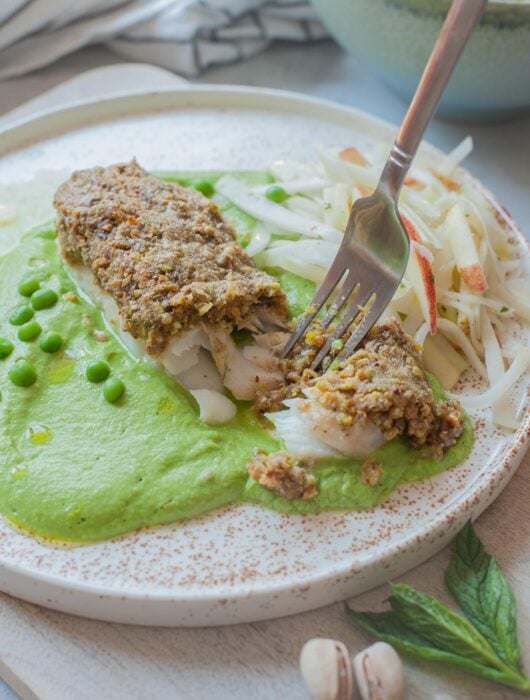 Pistachio crusted fish with mint puree and kohlrabi slaw on a white plate.