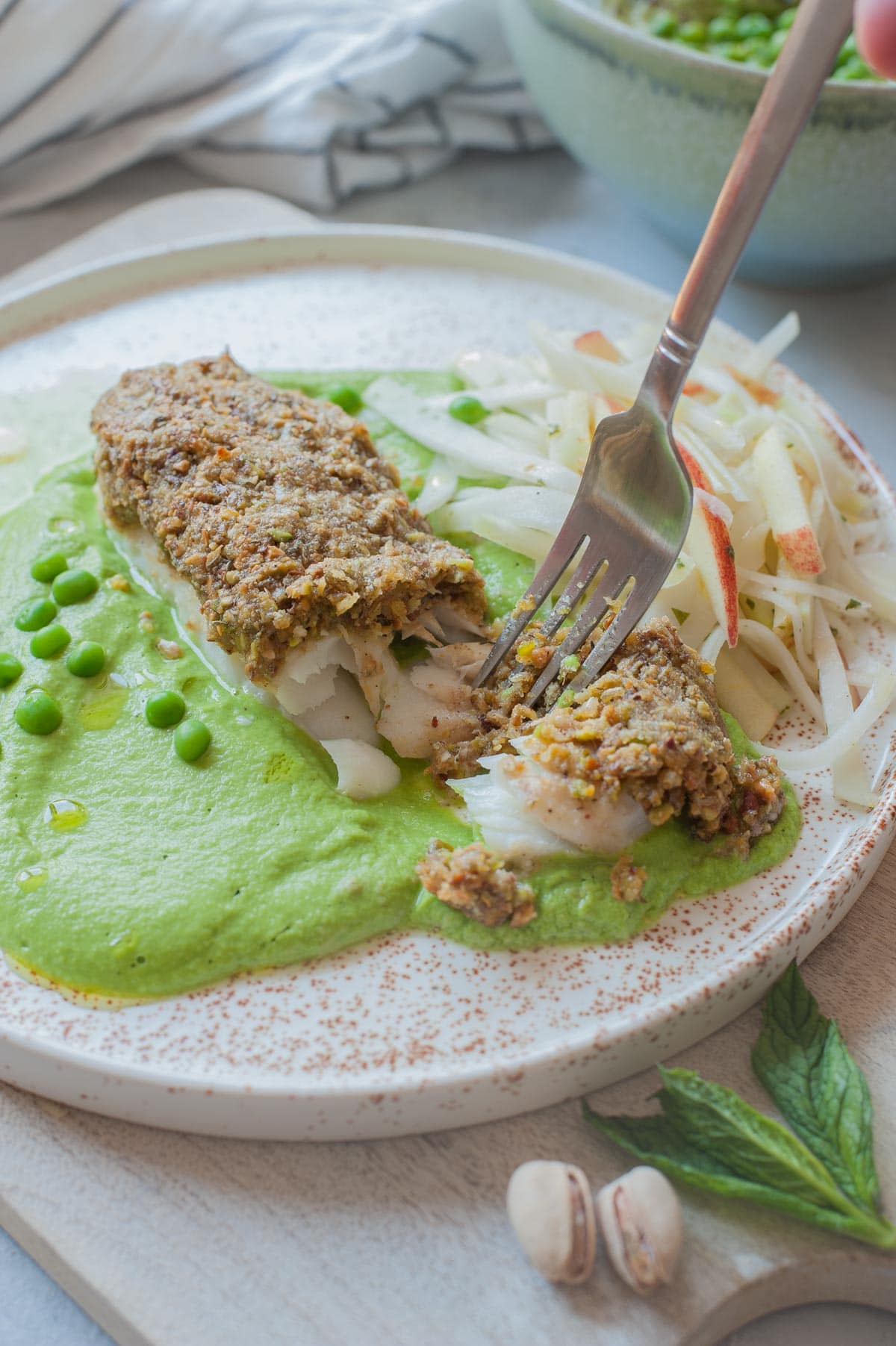 Pistachio crusted fish with pea puree and kohlrabi slaw on a white plate.