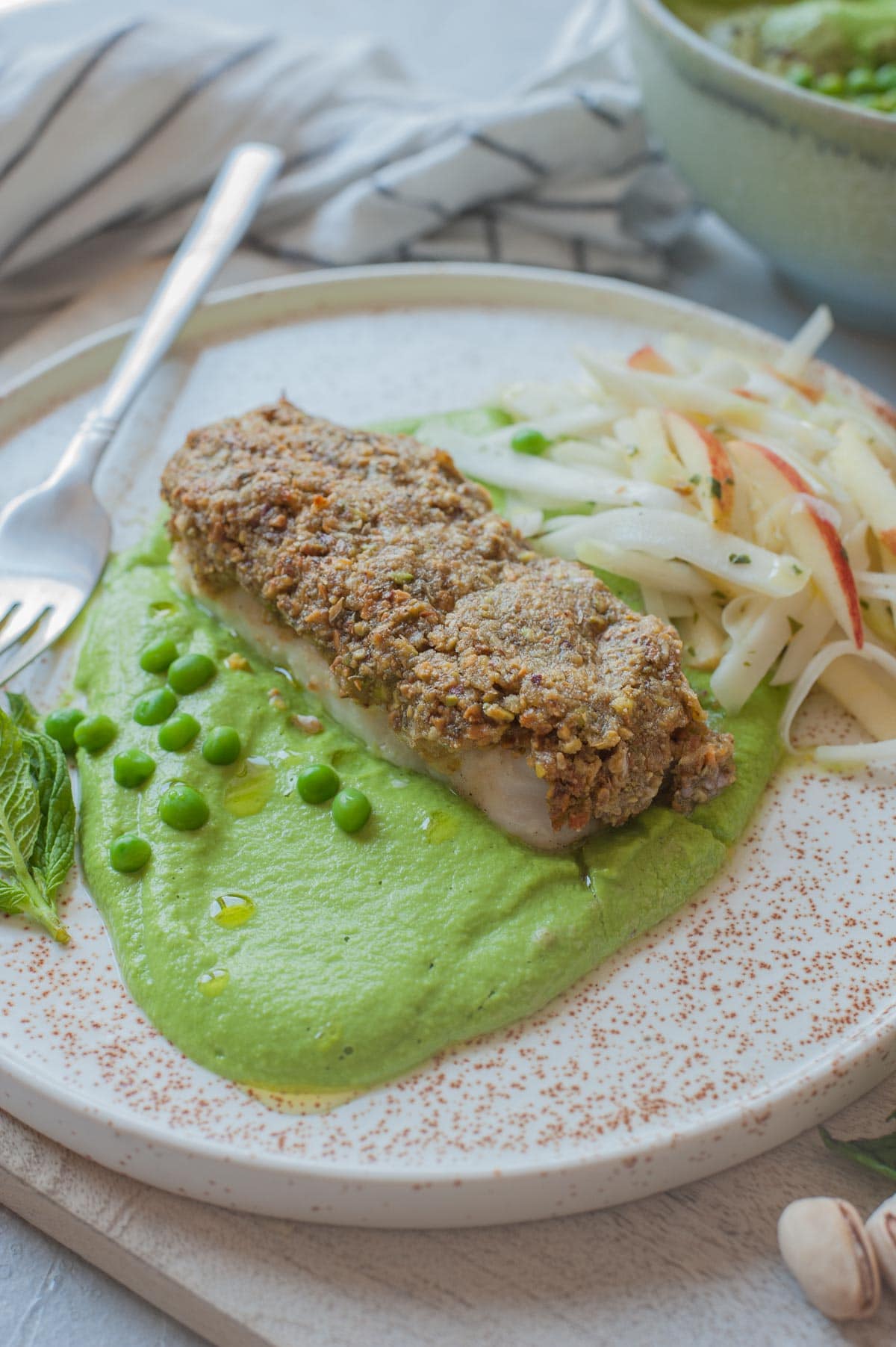 Pistachio crusted fish with pea puree and kohlrabi slaw on a white plate.