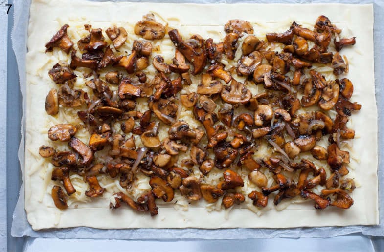 Sautéed mushrooms, onions, and shredded cheese on a puff pastry sheet.