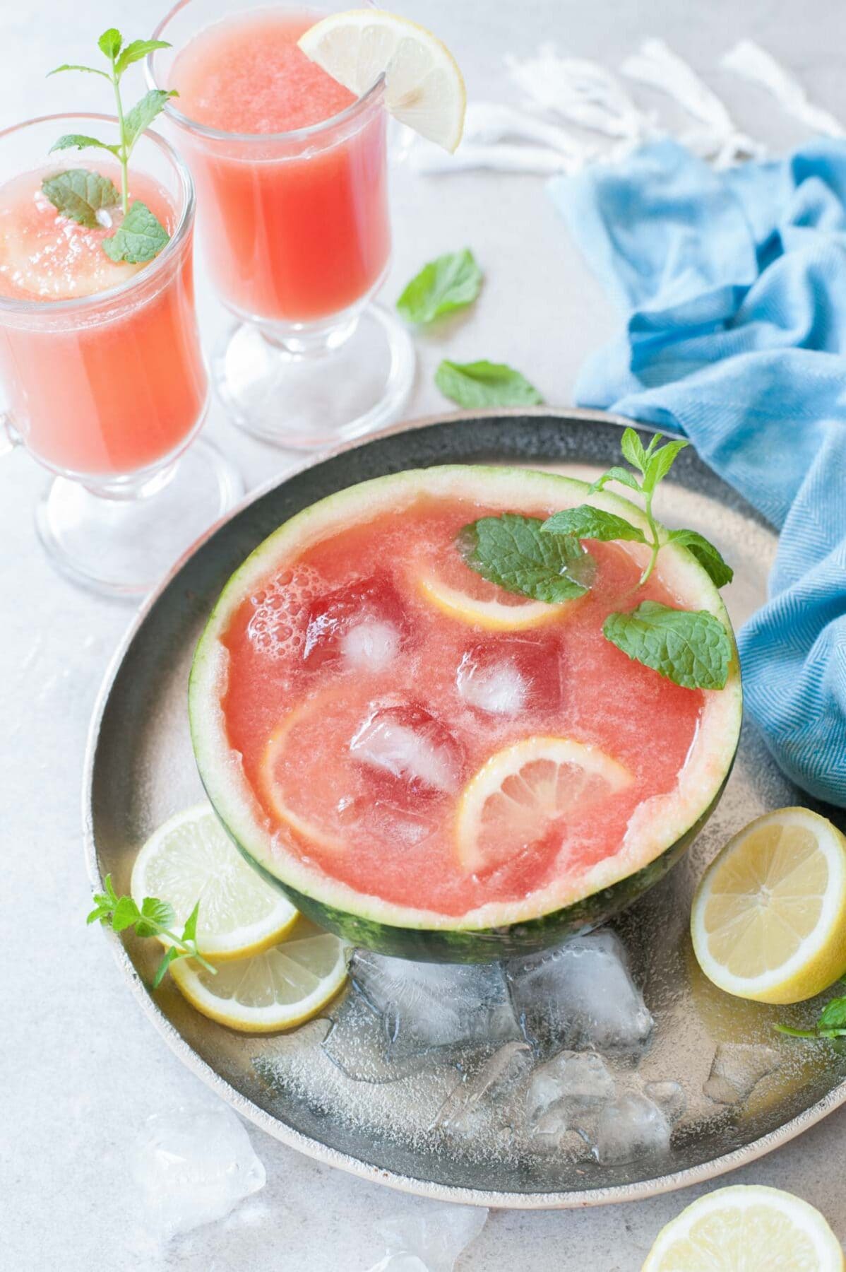 Watermelon half filled with watermelon mint lemonade. Two glasses with lemonade in the background.