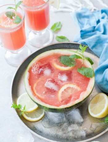 Watermelon mint lemonade in a watermelon half with ice cubes and lemon slices.