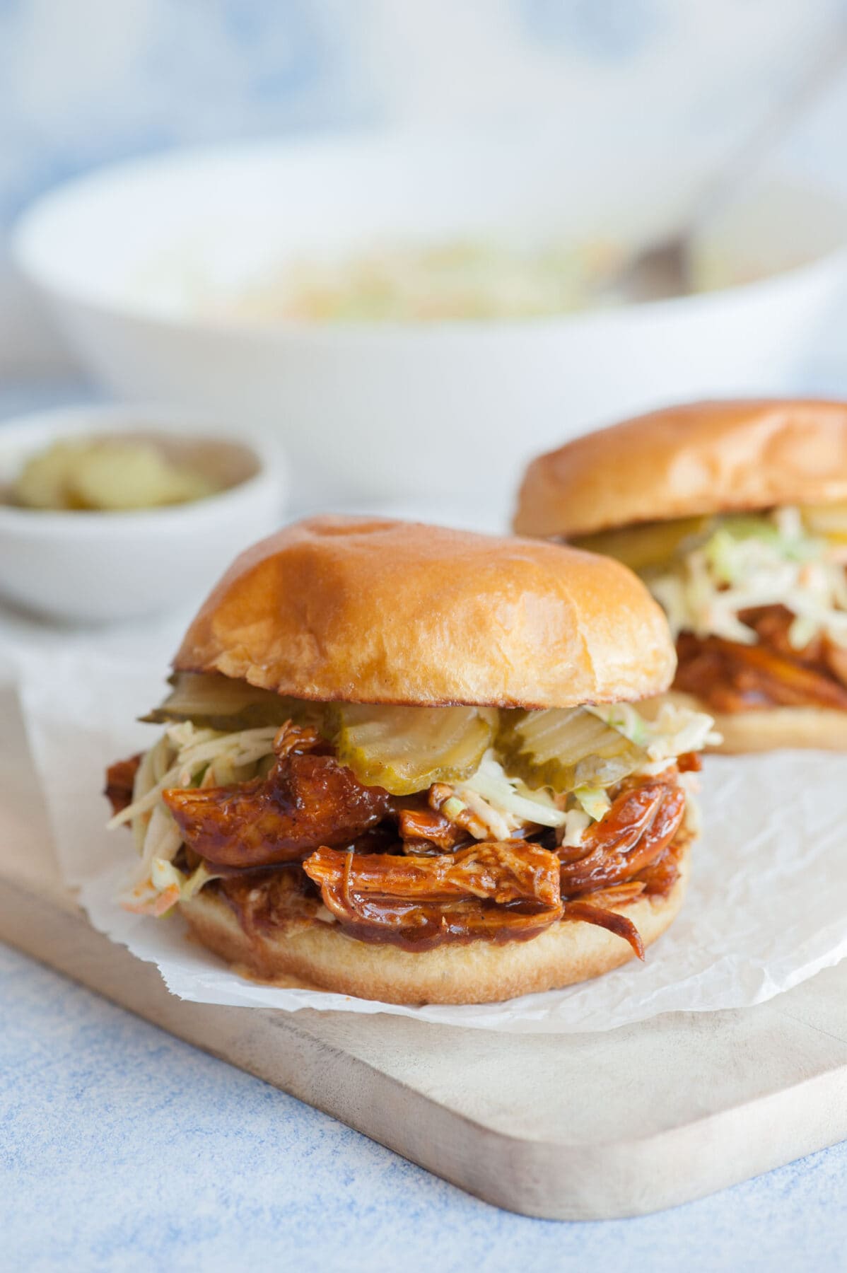 BBQ Pulled Chicken Sandwich on a piece of parchment paper on a white wooden board.