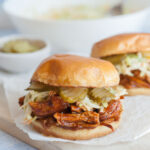 Bbq pulled chicken sandwich on a piece of parchment paper on a wooden board.