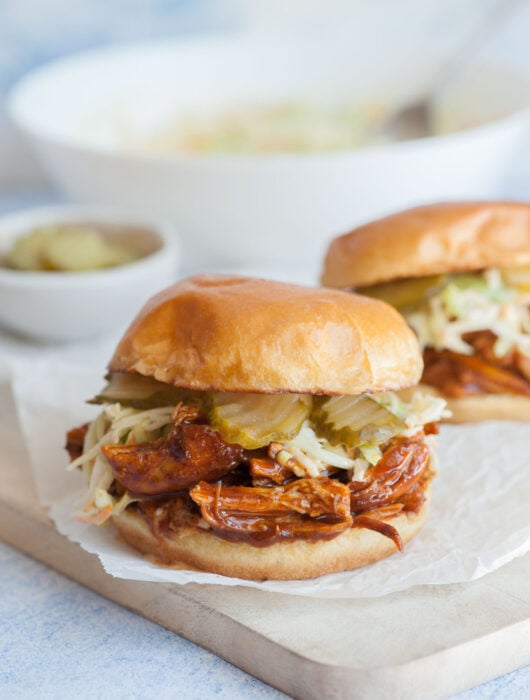 Bbq pulled chicken sandwich on a piece of parchment paper on a wooden board.