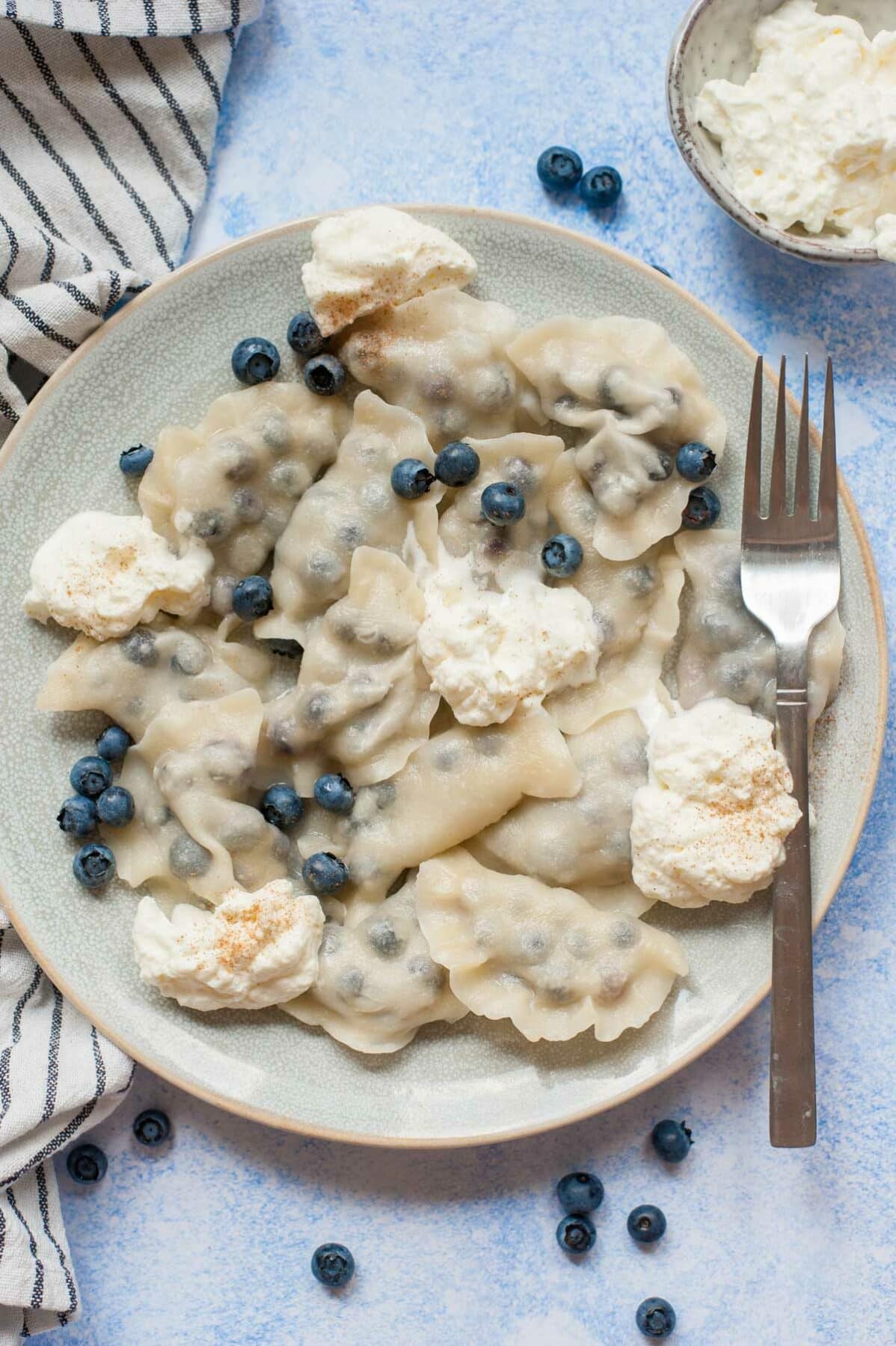 Blueberry pierogi served with fresh blueberries and whipped cream on a blue plate.