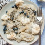 Blueberry pierogi served with fresh blueberries and whipped cream on a blue plate.