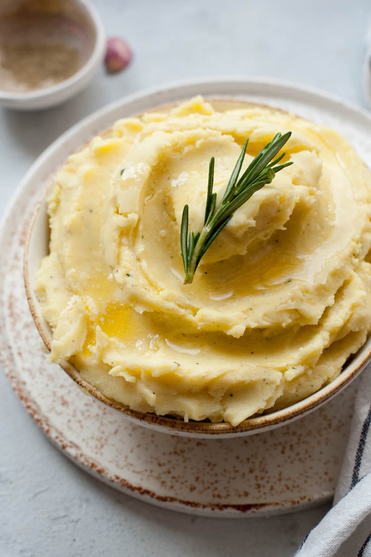 Cheddar mashed potatoes in a white bowl topped with a rosemary sprig.