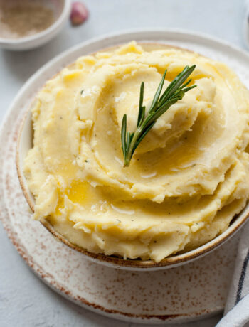 Cheddar mashed potatoes in a white bowl topped with a rosemary sprig.