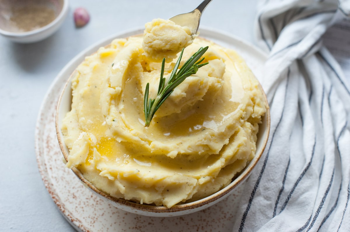 Cheddar mashed potatoes in a white bowl topped with a rosemary sprig.