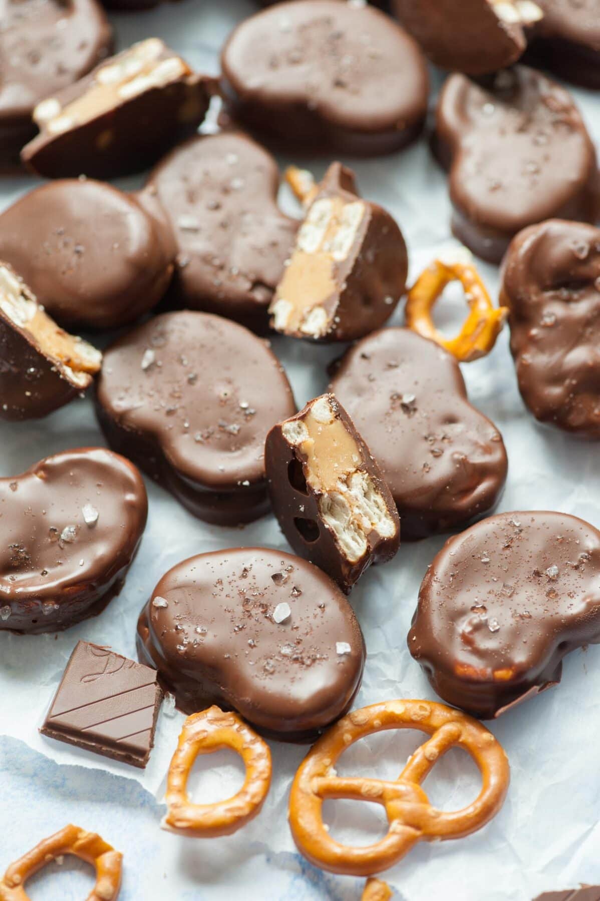 Chocolate peanut butter pretzels on a piece of parchment paper. Chocolate pieces and pretzels scattered around.