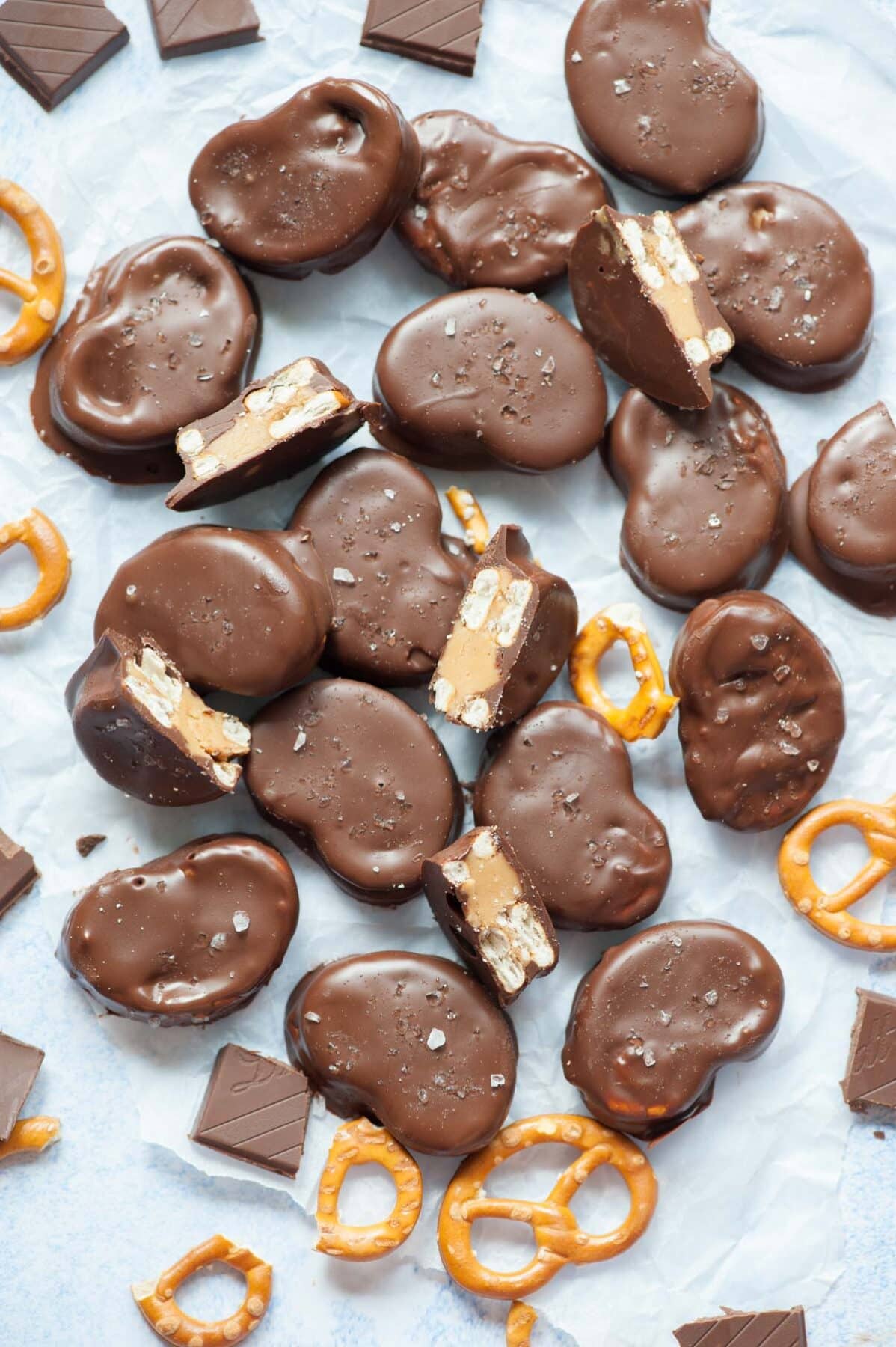 Chocolate peanut butter pretzels on a piece of parchment paper. Chocolate pieces and pretzels scattered around.