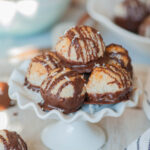 Chocolate-dipped coconut macaroons on a white cookie stand.