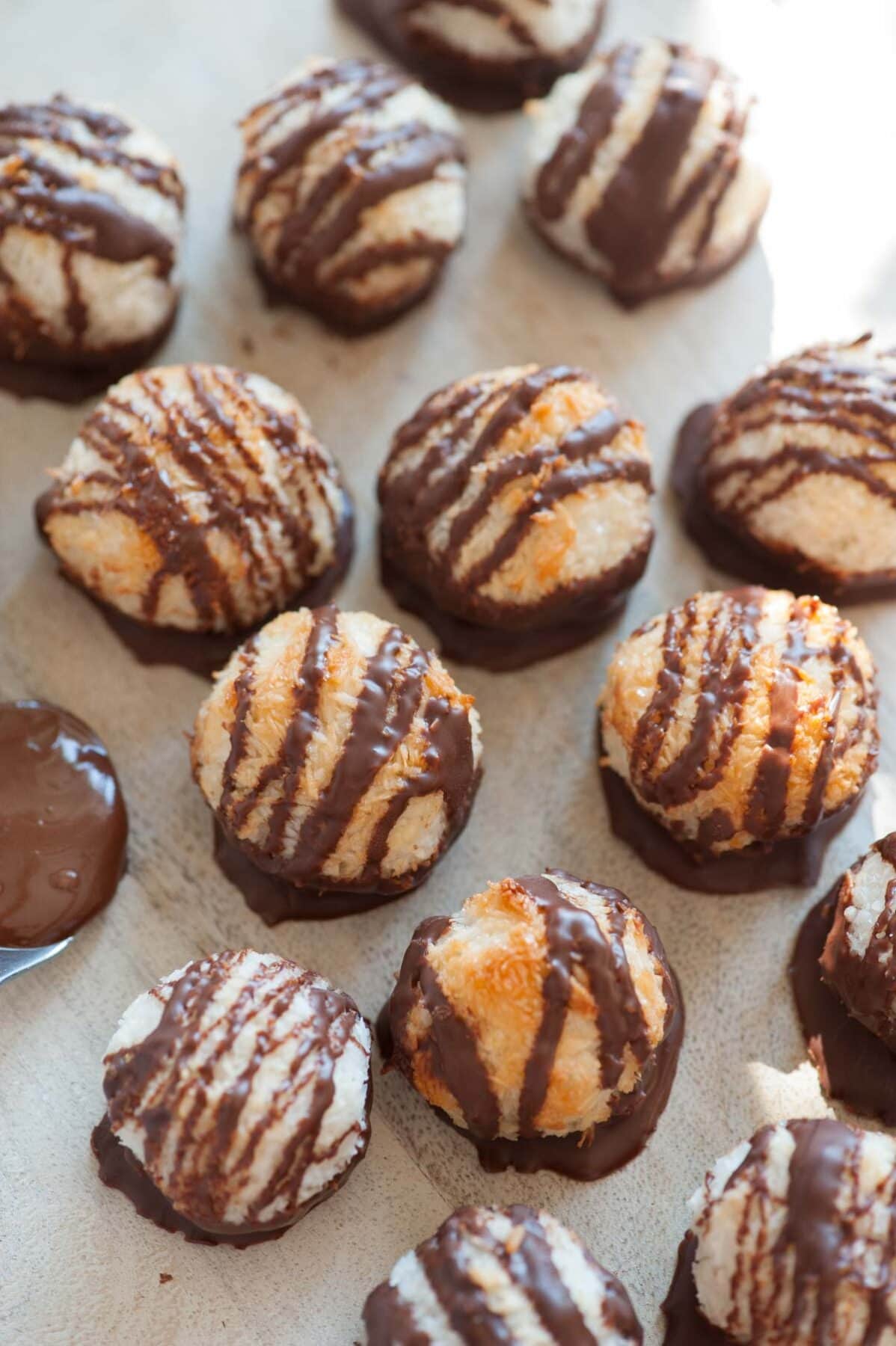 Chocolate dipped coconut macaroons on a beige wooden board.