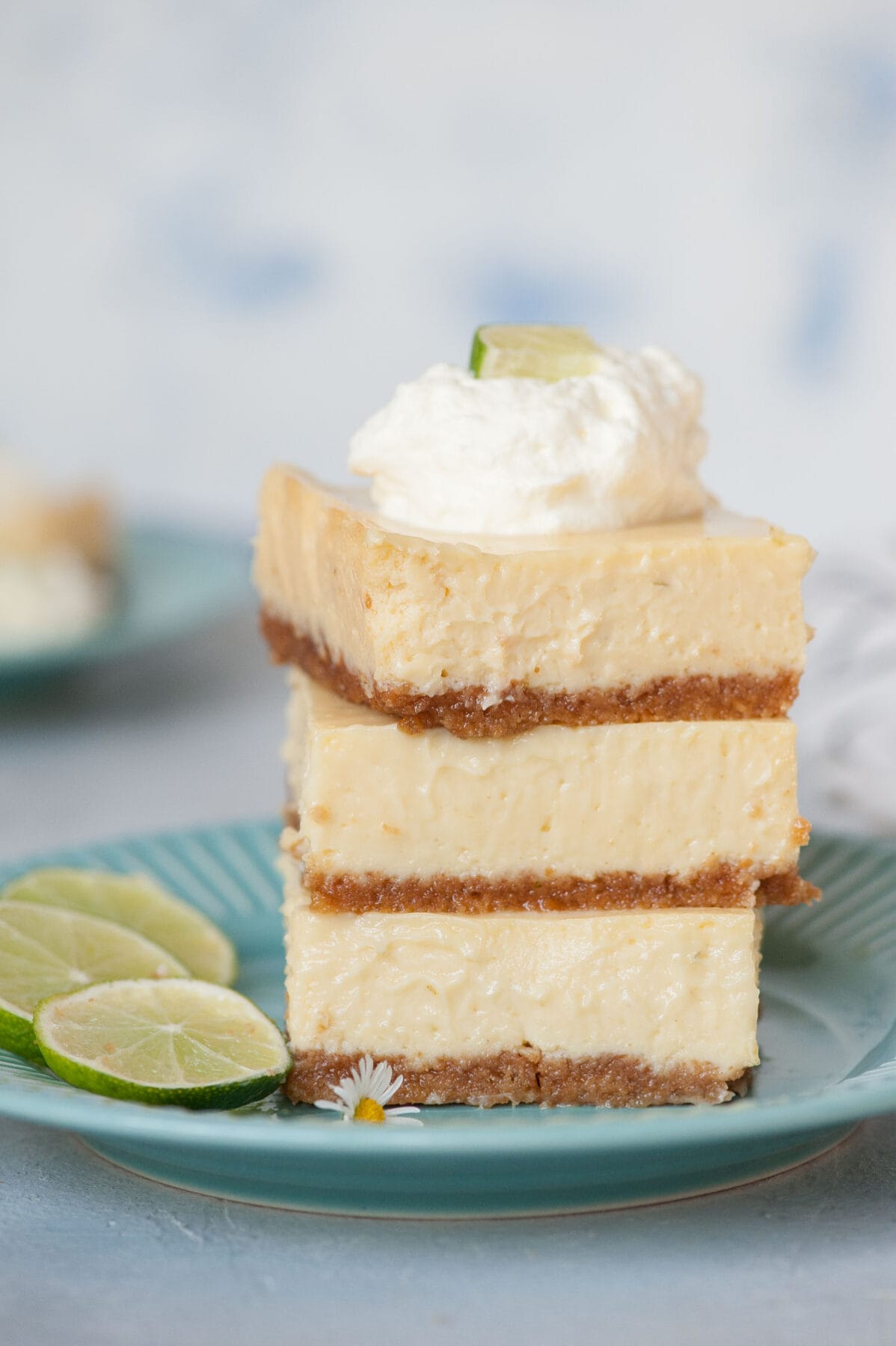 A stack of Key lime pie bars topped with whipped cream on a blue plate.