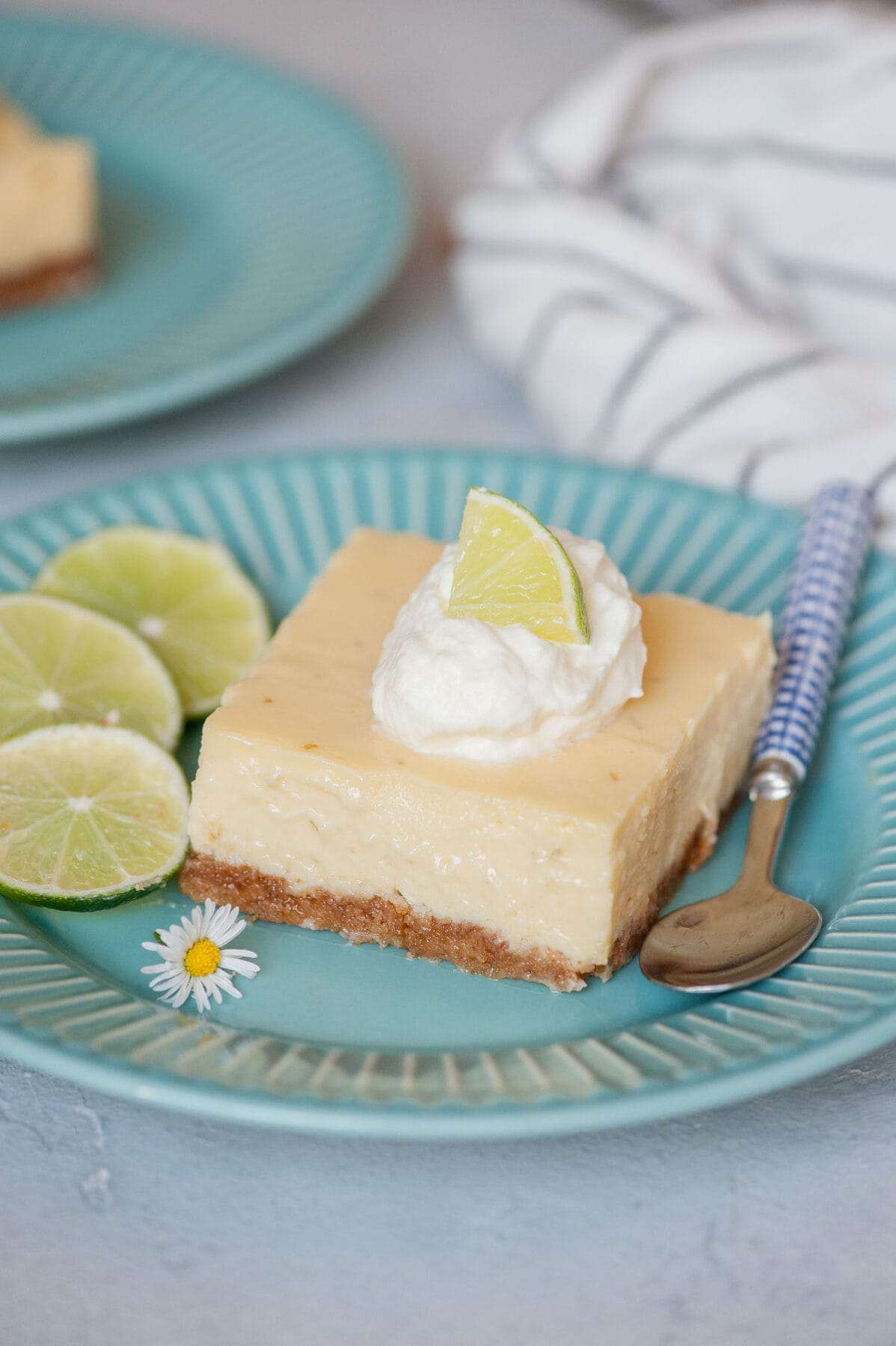 One Key lime pie bar topped with whipped cream and lime slices on a blue plate.