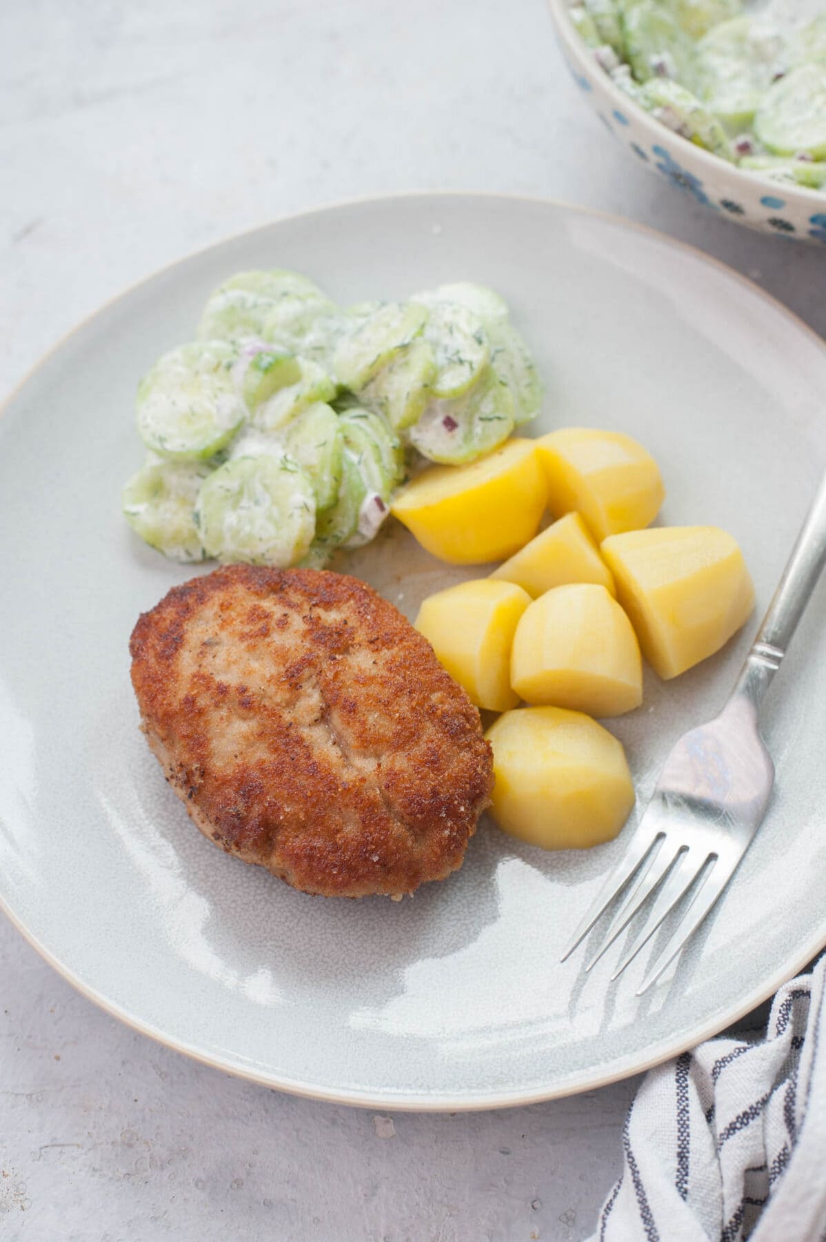 Kotlety mielone (Polish meat patties) on a blue plate with potatoes and cucumber salad.