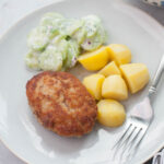 Ground pork patties, potatoes, and cucumber salad on a blue plate.