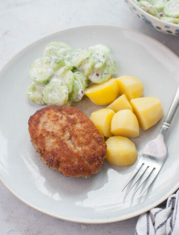 Ground pork patties, potatoes, and cucumber salad on a blue plate.