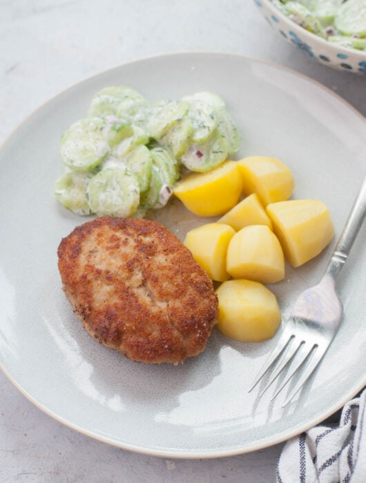 Ground pork patties, potatoes, and cucumber salad on a blue plate.