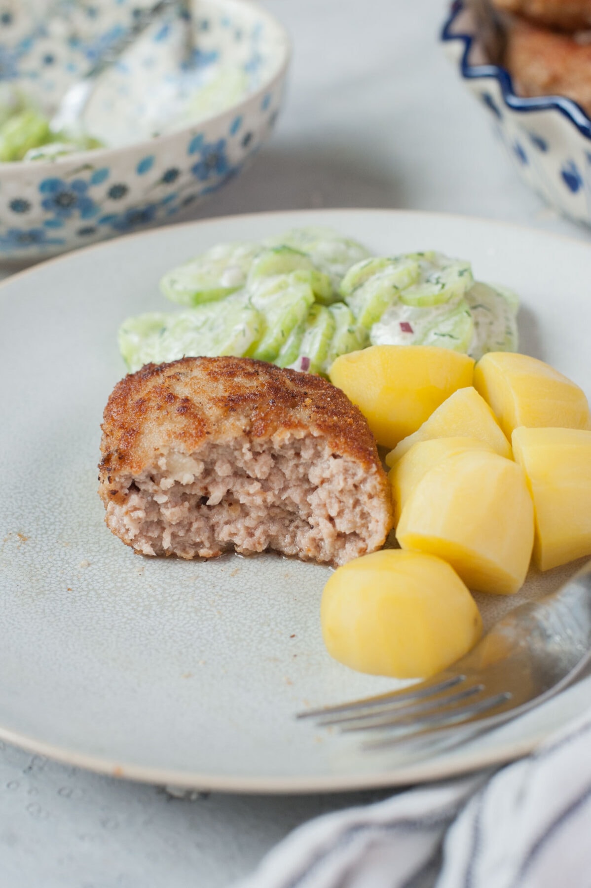 Kotlety mielone (Polish meat patties) on a blue plate with potatoes and cucumber salad.