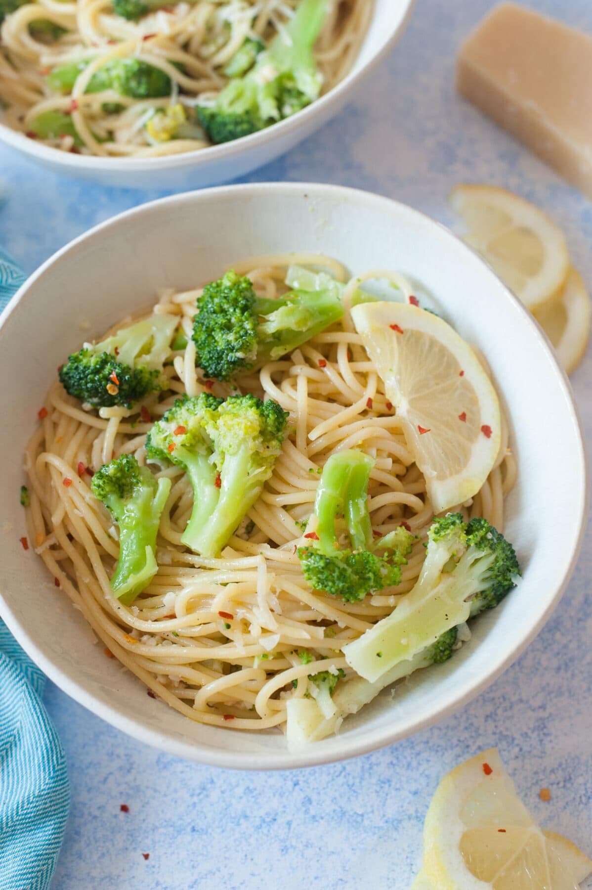 Lemon broccoli pasta in a white bowl. Lemon slices and parmesan cheese in the background.