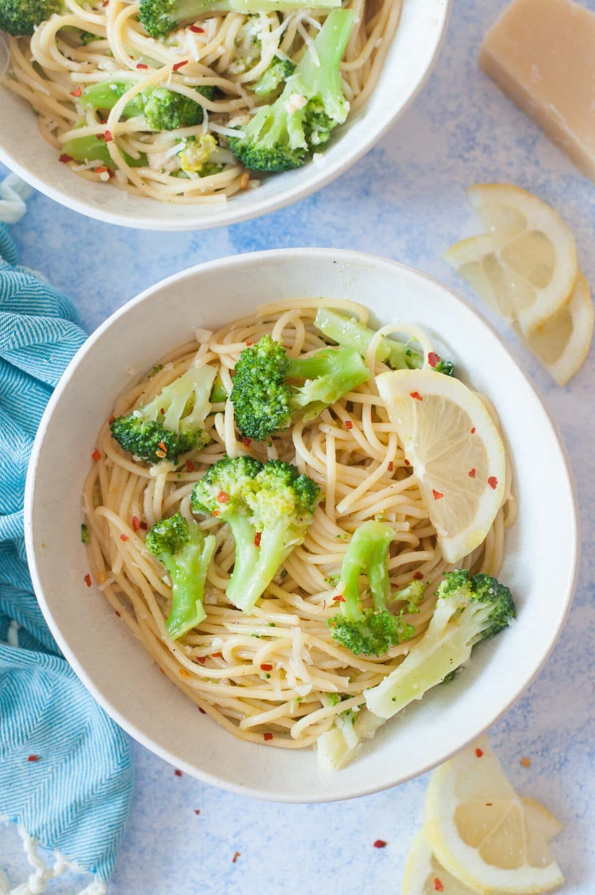 Lemon broccoli pasta in a white bowl. Lemon slices and parmesan cheese in the background.