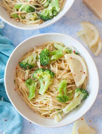 Lemon broccoli pasta in a white bowl. Lemon slices and parmesan cheese in the background.