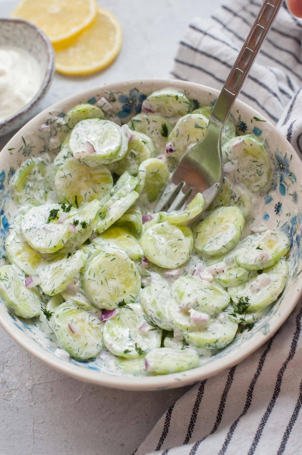 Mizeria (Polish cucumber salad) in a white bowl is being stuck on a fork.