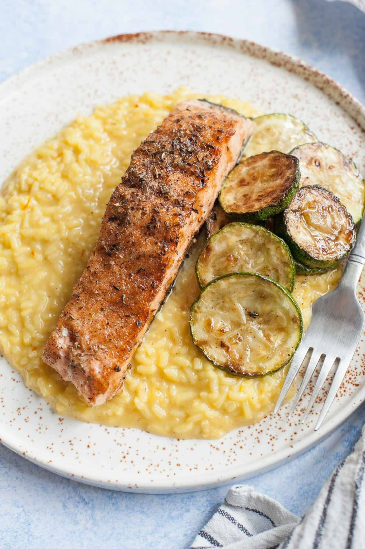 Saffron risotto with grilled salmon and zucchini on a white plate.