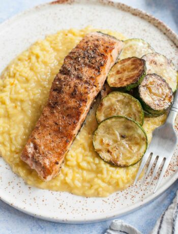 Saffron risotto with grilled salmon and zucchini on a white plate.