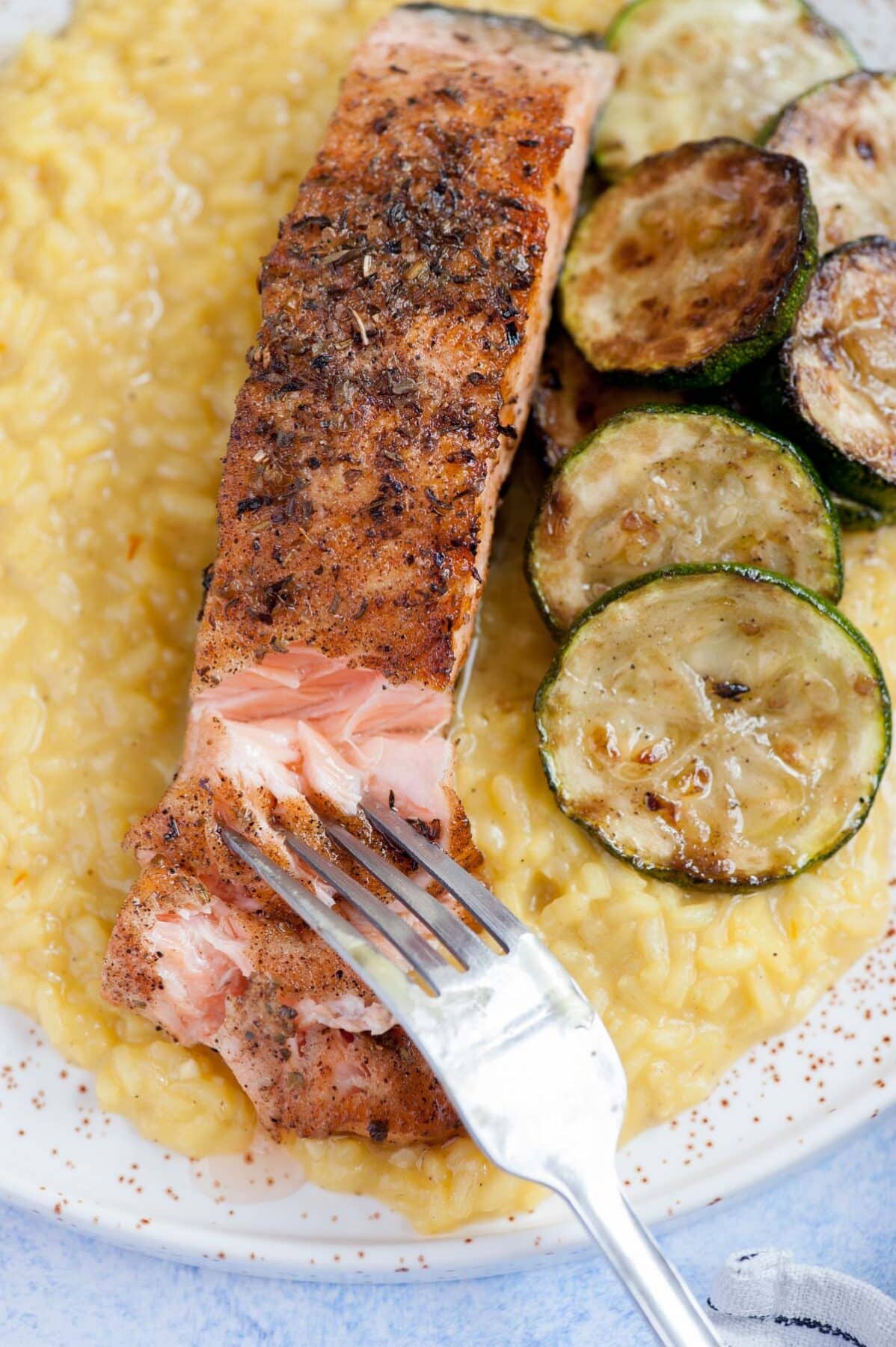 A close up picture of saffron risotto with grilled salmon and zucchini.