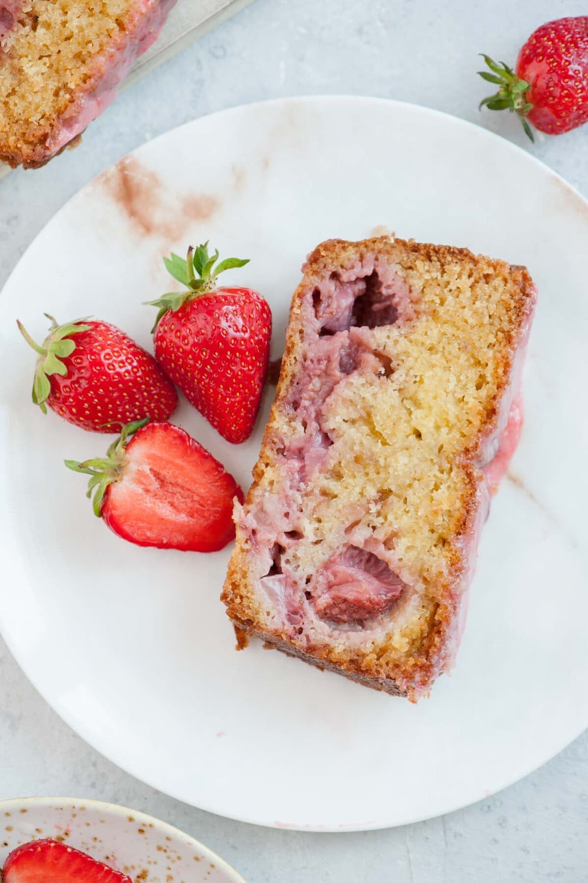 A slice of strawberry bread on a white plate with strawberries on the side.