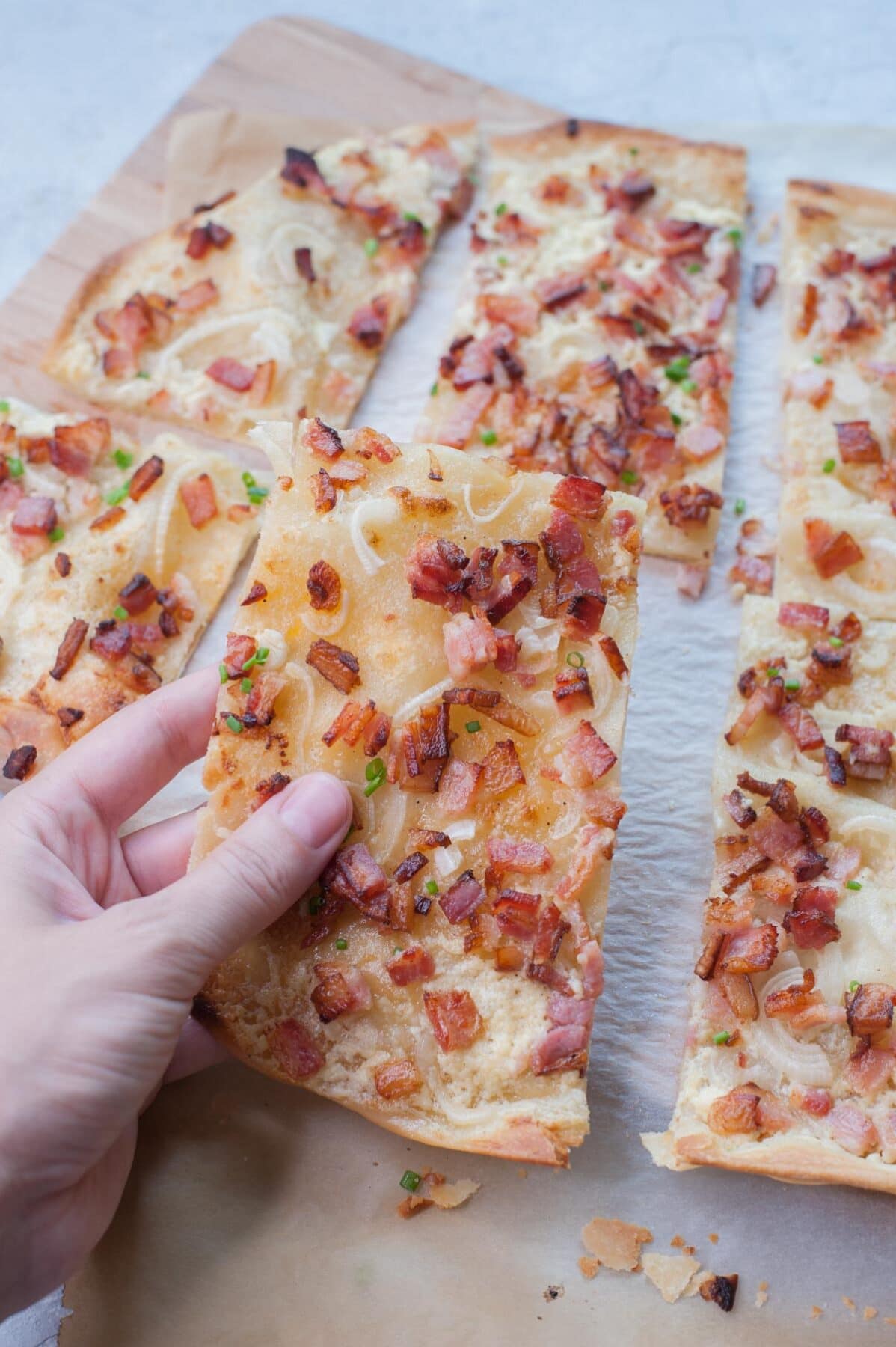 A piece of Flammkuchen is being held in a hand.