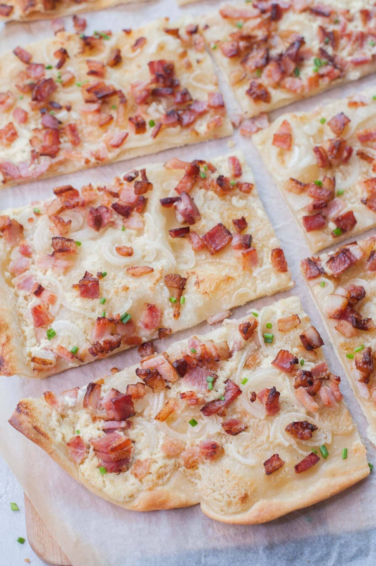 Flammkuchen cut into squares on a piece of parchment paper.