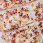 Flammkuchen cut into squares on a piece of parchment paper.