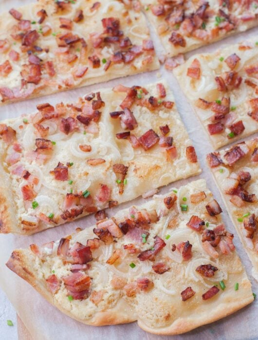 Flammkuchen cut into squares on a piece of parchment paper.