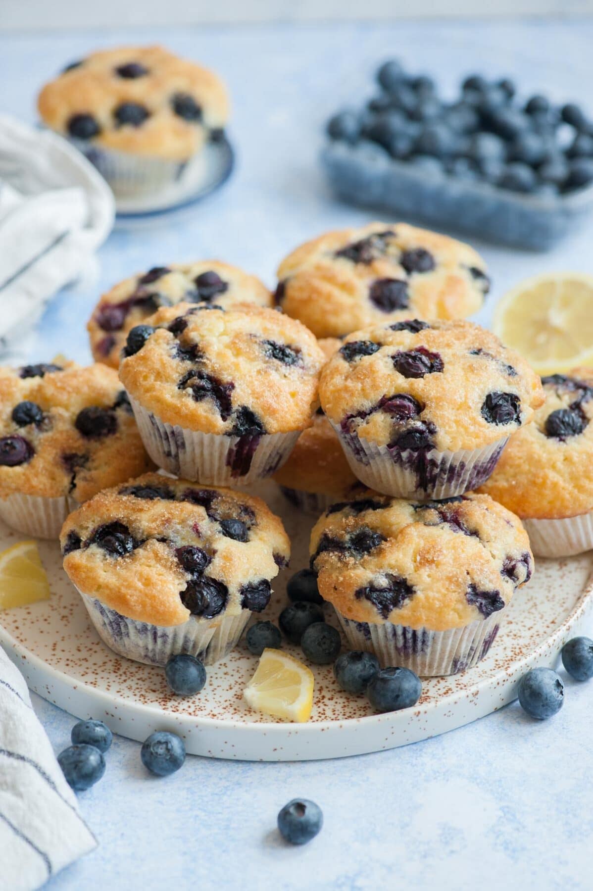 Blueberry muffins on a white plate. Blueberries and lemon slices scattered around.