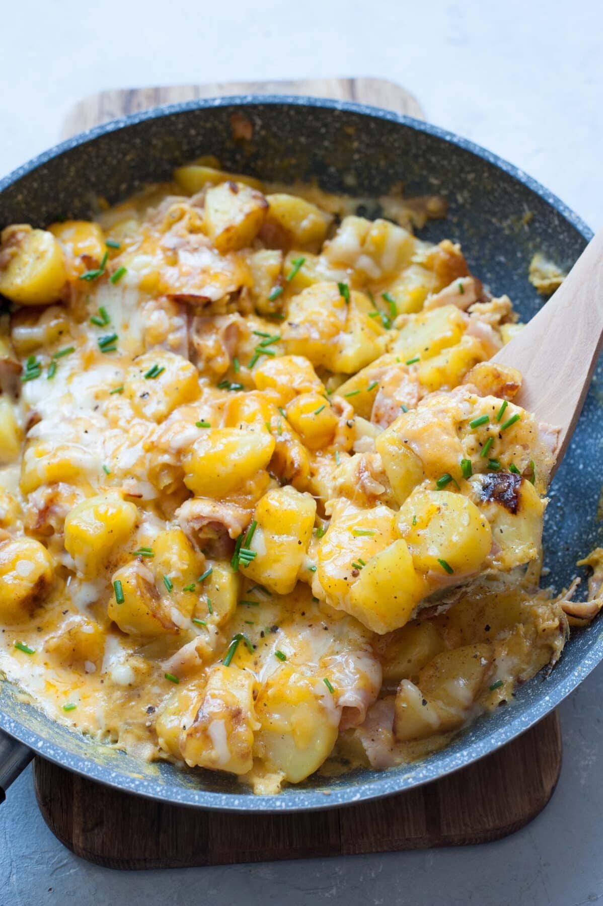 Potato egg scramble topped with melted cheese and chives in a grey pan.