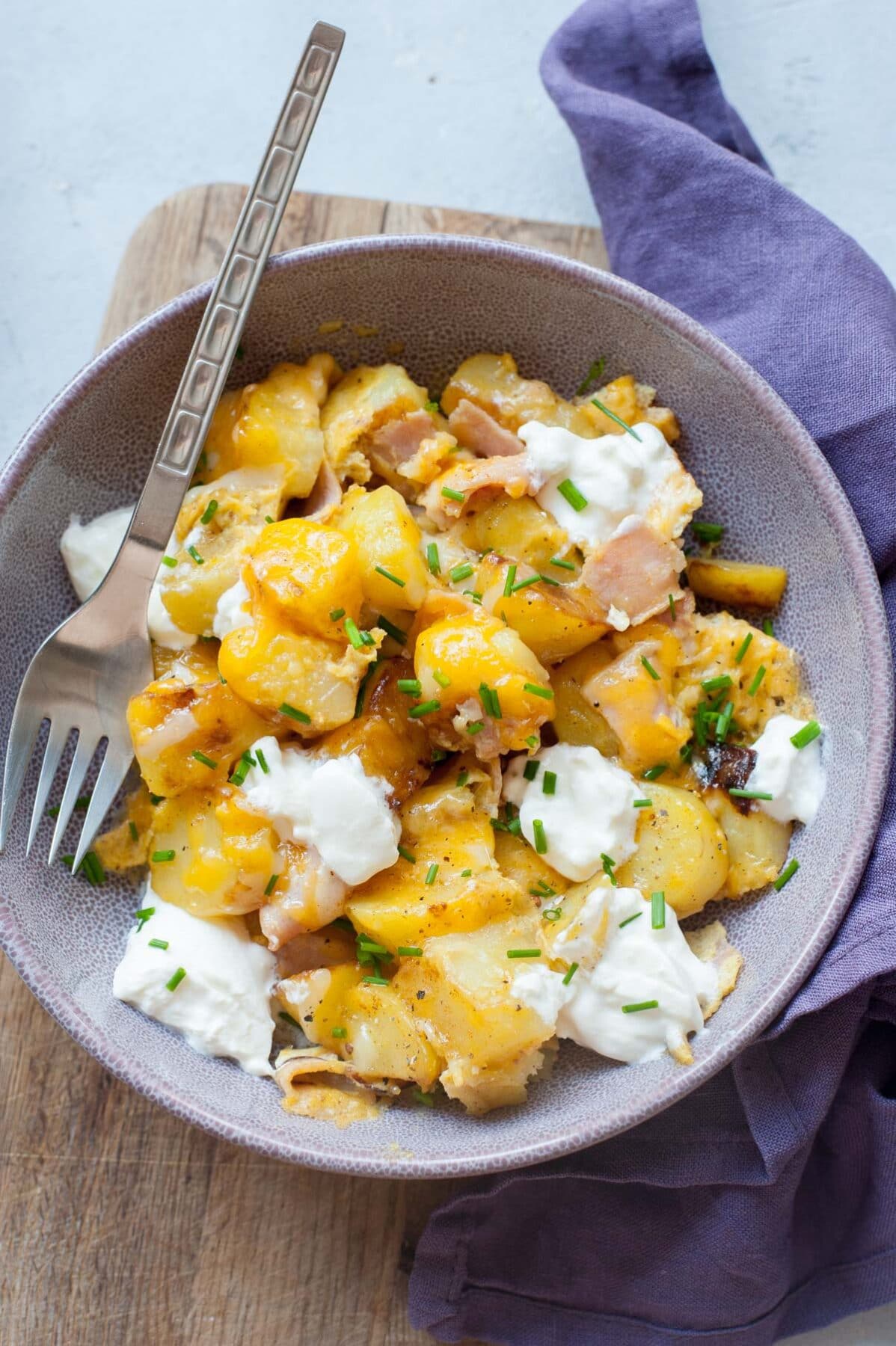 Potato egg scramble topped with cheese, sour cream, and chives in a violet bowl.