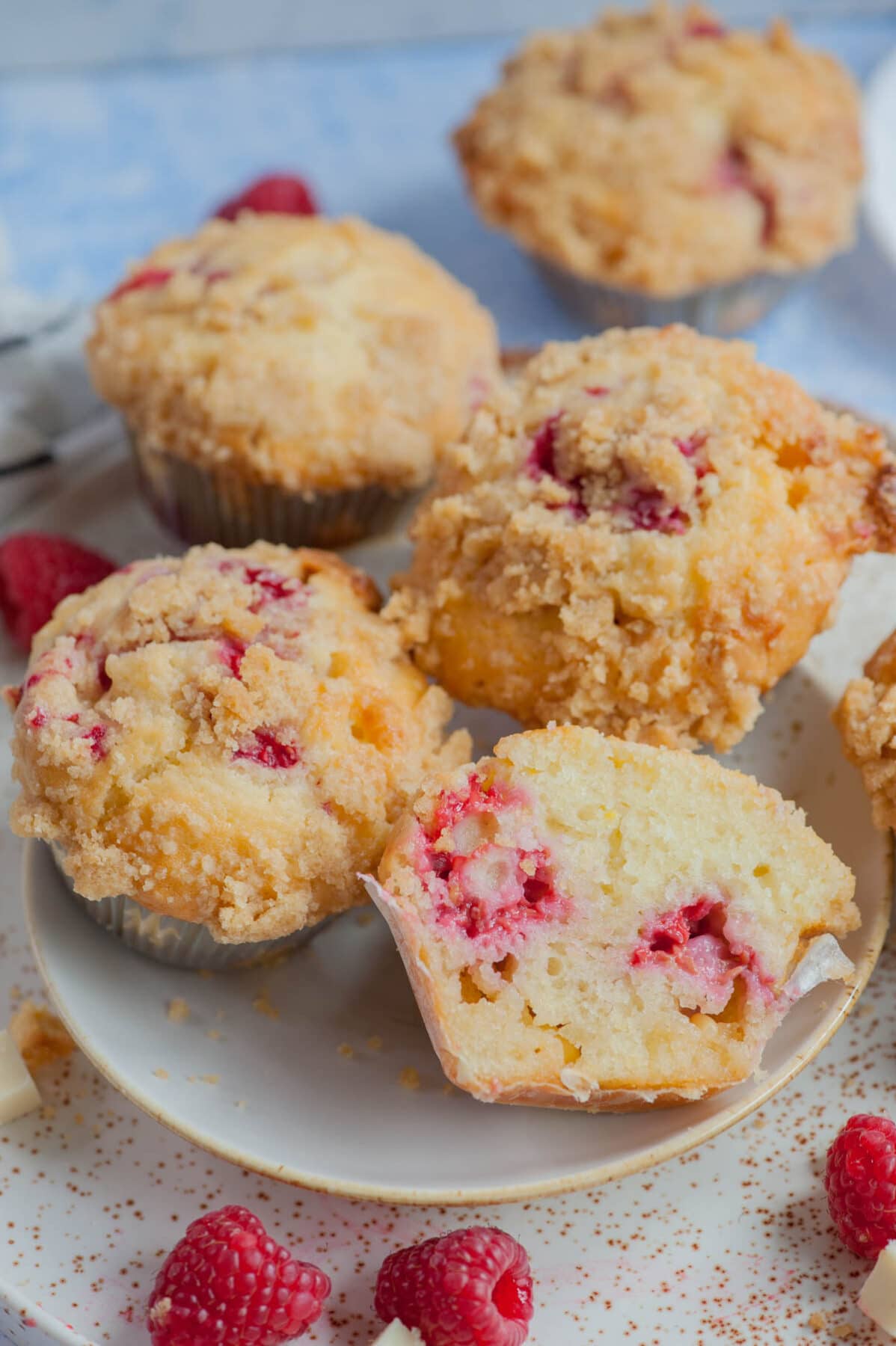 Raspberry muffins on a white plate. Raspberries and white chocolate chunks scattered around.