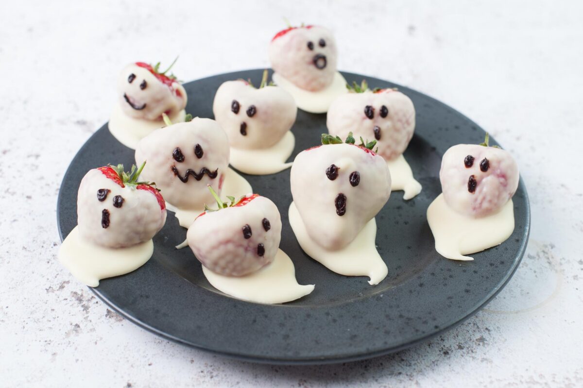 White chocolate covered strawberries (Strawberry ghosts) on a black plate.